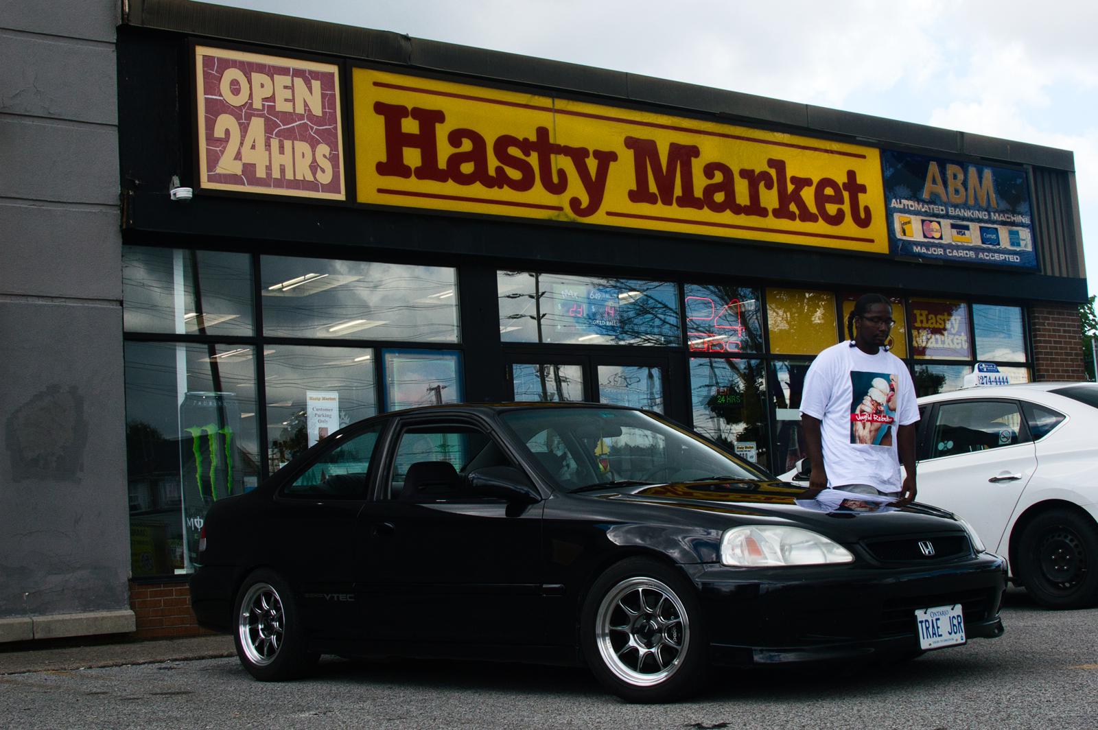 Man with Joyful Rebellion T shirt next to car outside of Hasty Market